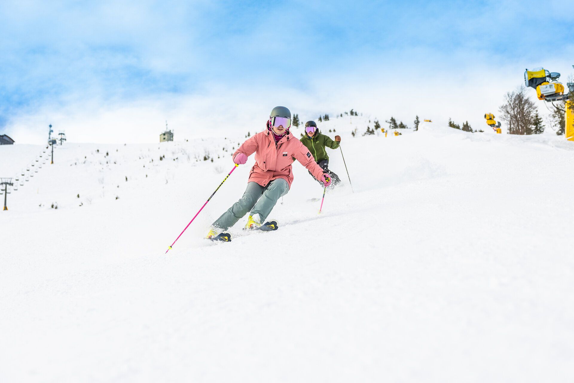 Zwei Skifahrer gleiten elegant über die schneebedeckten Pisten, während die strahlende Wintersonne den glitzernden Schnee erleuchtet. Die frische Bergluft und die atemberaubende Aussicht auf die umliegenden Gipfel schaffen eine unvergessliche Atmosphäre für Wintersportliebhaber.