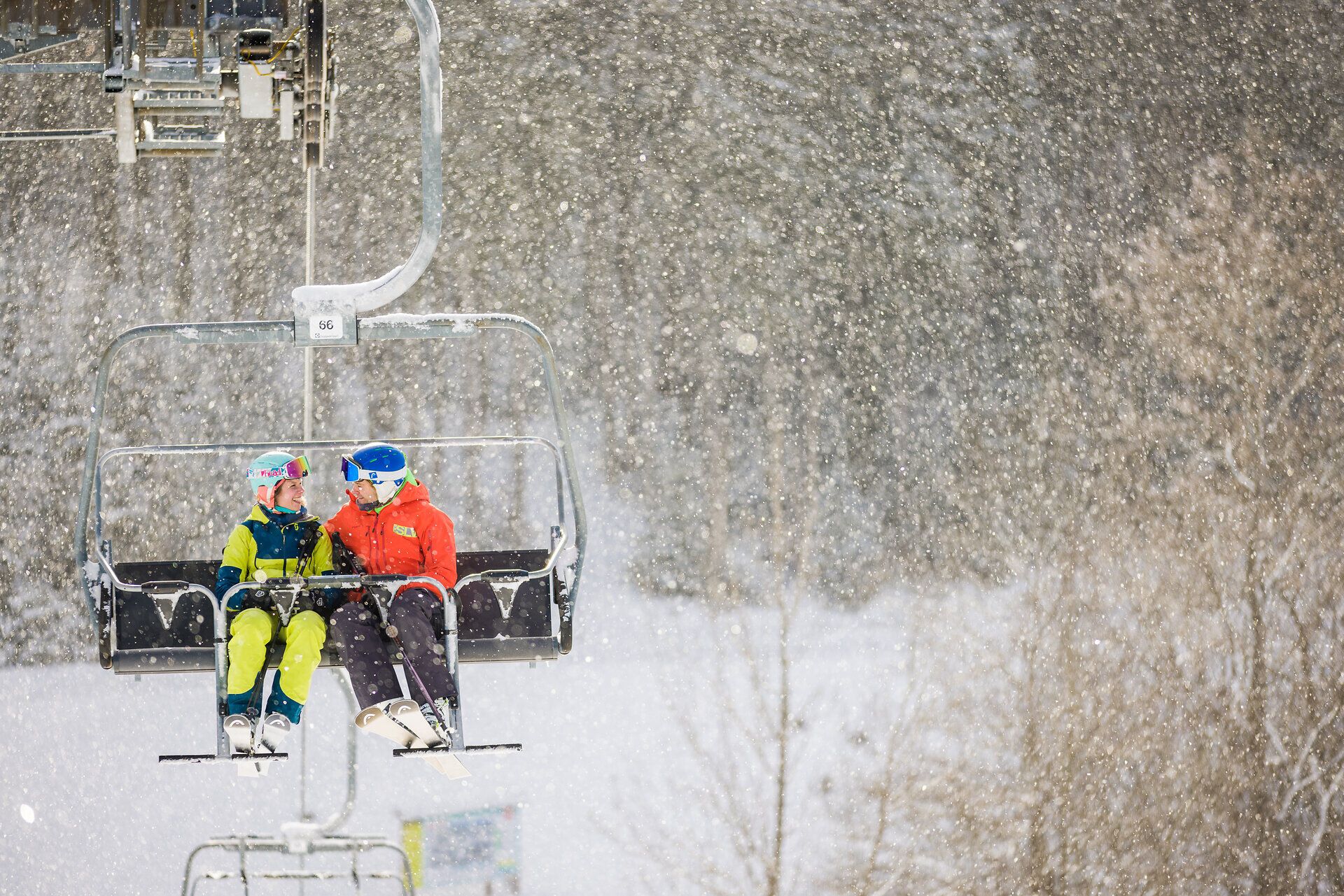 Ein Paar genießt die winterliche Idylle auf einem Sessellift, während sanfte Schneeflocken um sie herumtanzen. Die verschneiten Berge bieten eine atemberaubende Kulisse für unvergessliche Momente im Winterurlaub. Hier wird die Freude am Skifahren und die Romantik der Natur perfekt vereint.
