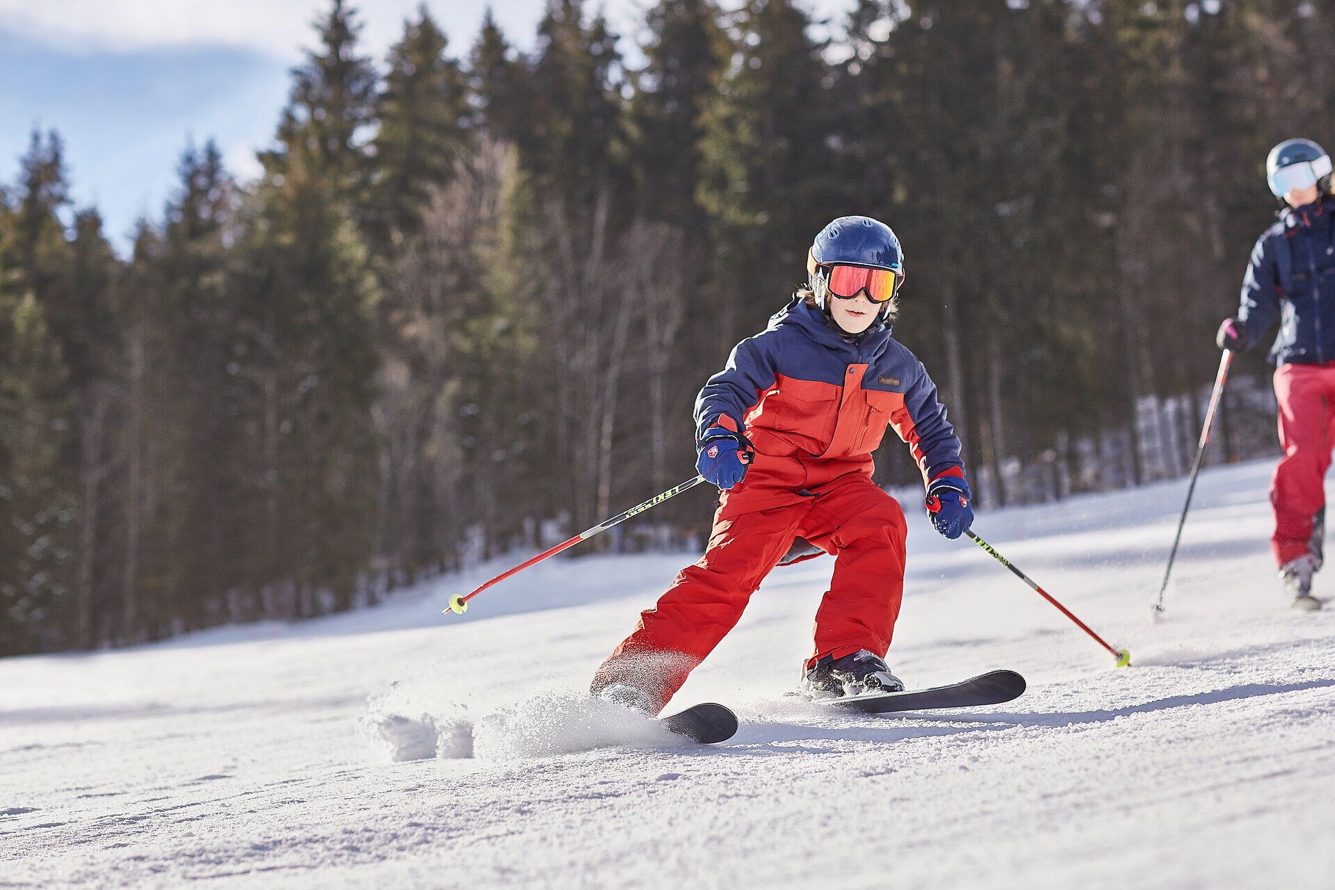 Ein fröhliches Kind gleitet mit Schwung über die schneebedeckten Pisten, während die strahlende Wintersonne den glitzernden Schnee erleuchtet. Umgeben von majestätischen Bergen und dichten Wäldern, wird hier der Wintertraum lebendig. Die frische, kalte Luft und das Lachen der Skifahrer schaffen eine unvergessliche Atmosphäre.