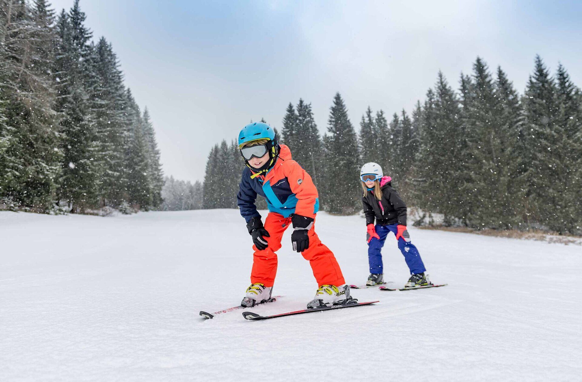 Zwei fröhliche Kinder gleiten mit Begeisterung über die schneebedeckten Pisten, umgeben von majestätischen Tannen. Der Winterzauber in Karlstift lädt dazu ein, die frische Bergluft zu genießen und unvergessliche Momente im Schnee zu erleben.