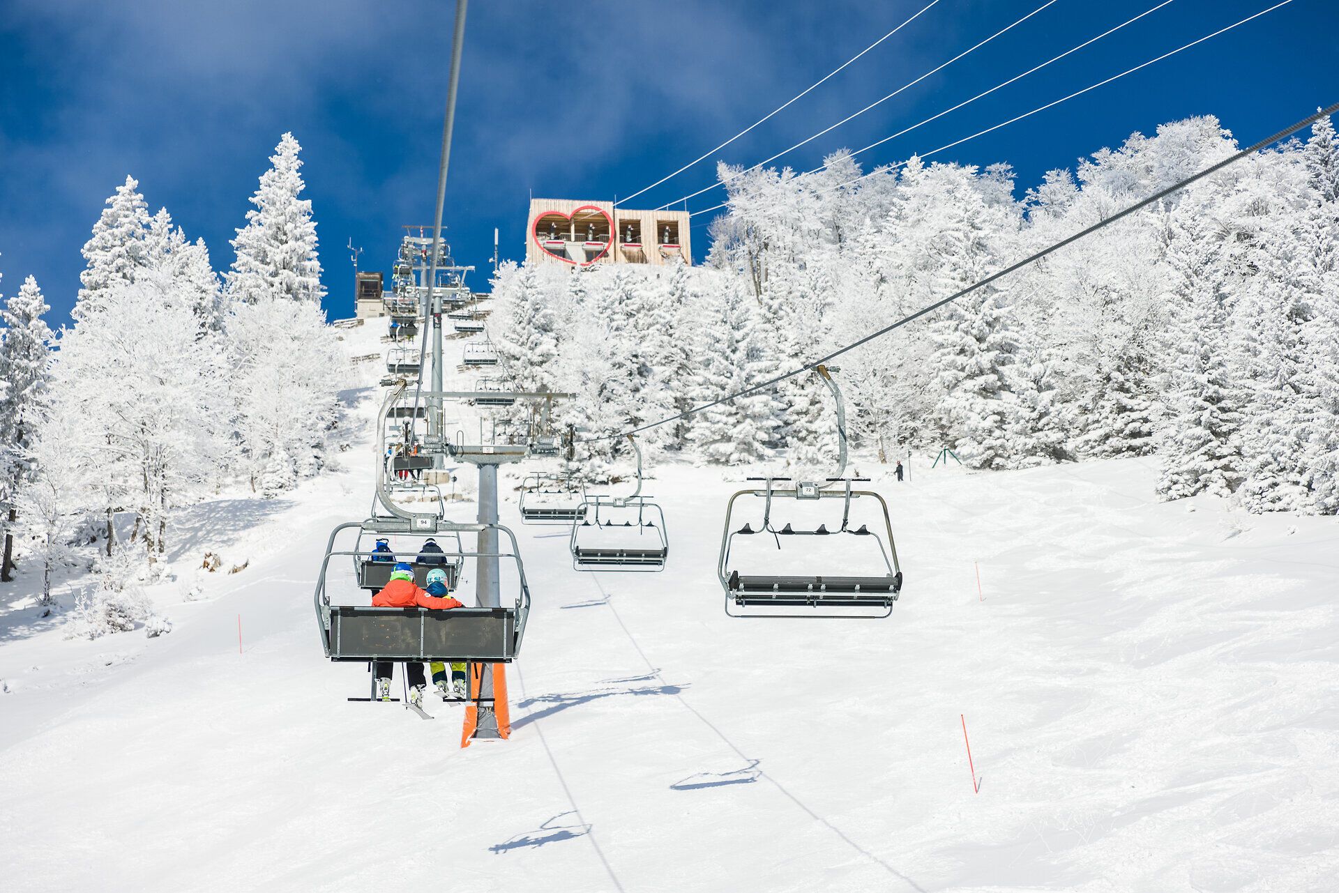 Die glitzernde Schneedecke erstreckt sich über die sanften Hügel, während der Sessellift gemächlich die Skifahrer zu neuen Abenteuern hinaufzieht. Umgeben von schneebedeckten Tannen und strahlend blauem Himmel, erleben die Besucher hier den Winter in seiner schönsten Form.