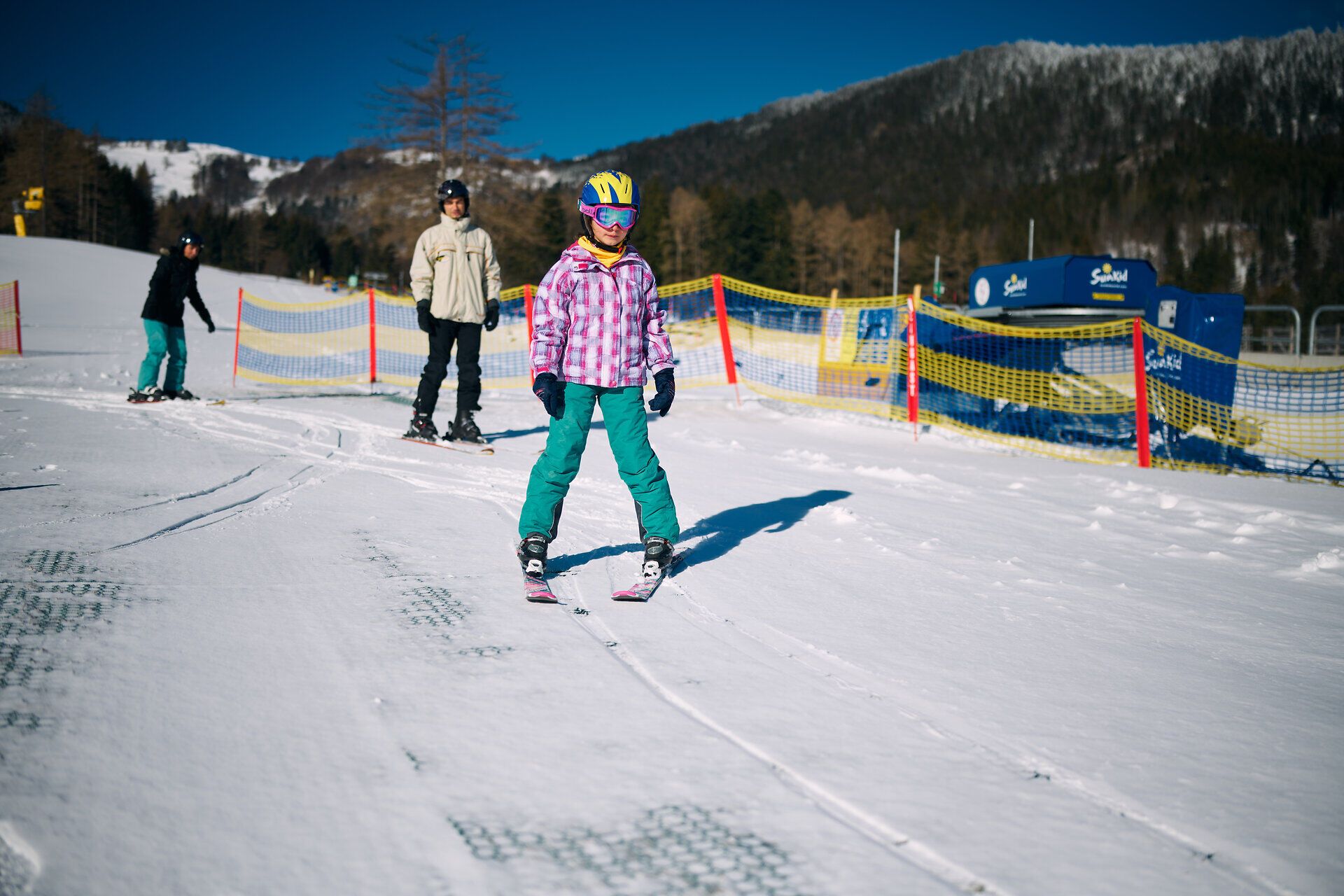 Ein strahlend blauer Himmel umrahmt die fröhlichen Skifahrer, die sich auf den sanften Hängen des Schneeberglands vergnügen. Die Kinder gleiten mit Begeisterung über den glitzernden Schnee, während die frische Bergluft ihre Gesichter erhellt. Hier wird der Winter zum unvergesslichen Erlebnis für die ganze Familie.