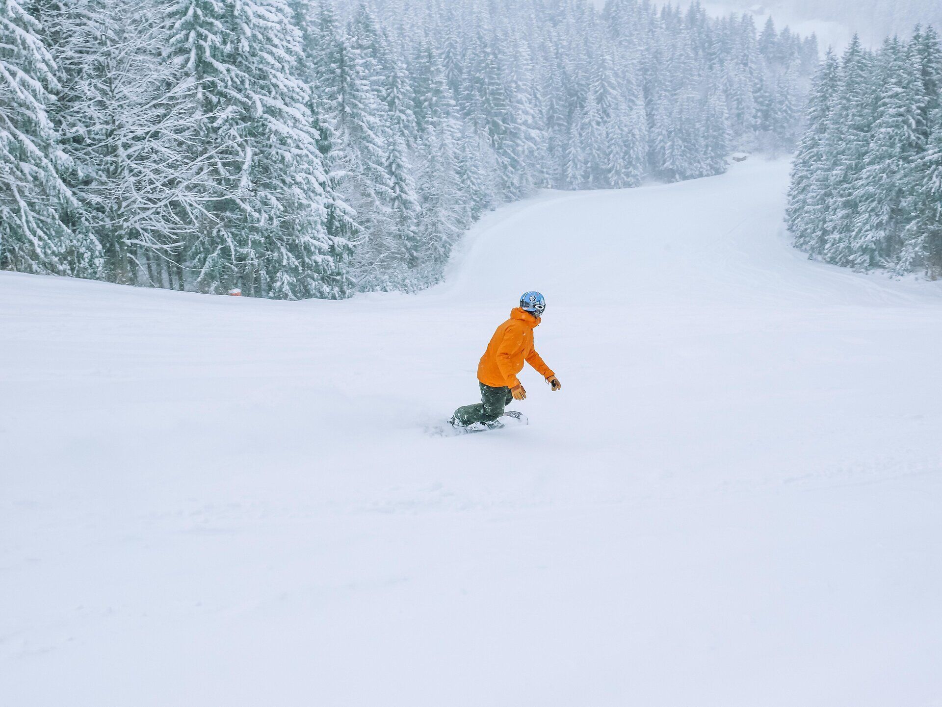 Ein strahlend orangefarbener Skifahrer gleitet durch den frischen, pulvrigen Schnee, umgeben von majestätischen, schneebedeckten Bäumen. Die ruhige Winterlandschaft lädt dazu ein, die klare, kalte Luft zu genießen und die Schönheit der Natur zu erleben. Hier in den Alpen wird der Winter zum unvergesslichen Abenteuer.